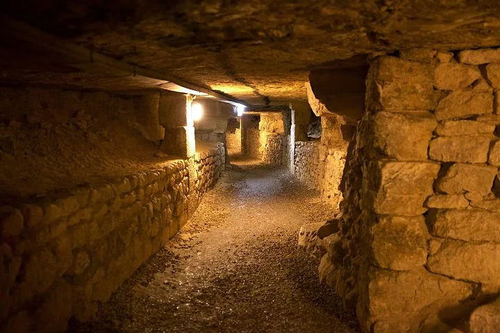 Un tunnel en pierre vide et doucement éclairé, au cœur des Catacombes de Paris.
