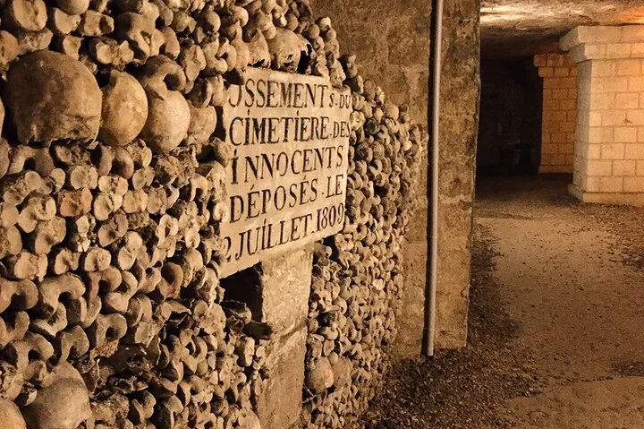 A stone sign set into a wall of skulls and bones along a walkway.