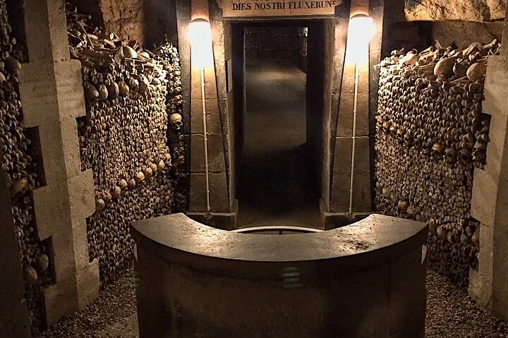 A stone structure at an entranceway flanked by walls of skulls and bones.